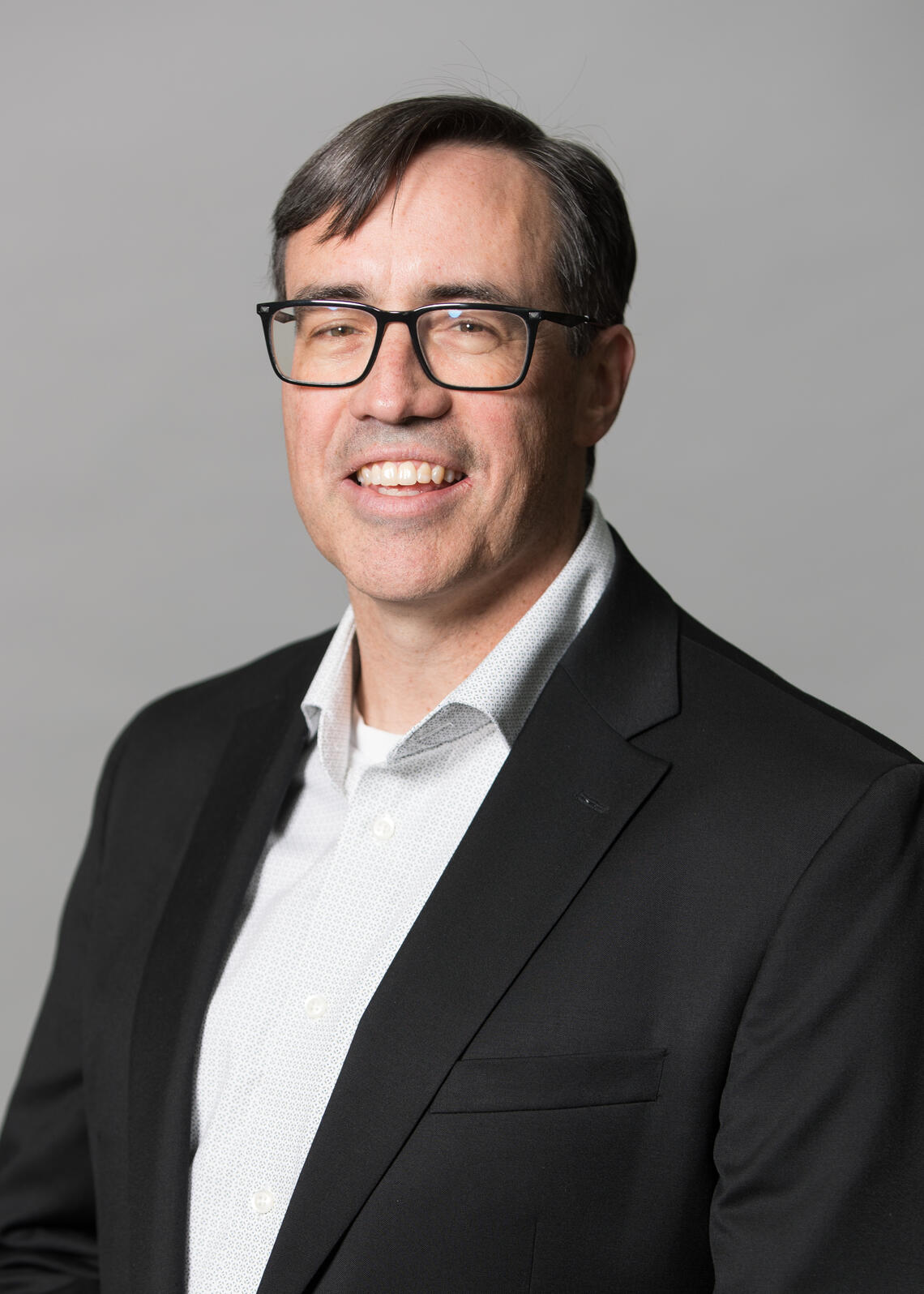 A man in a black suit and glasses smiles at the camera