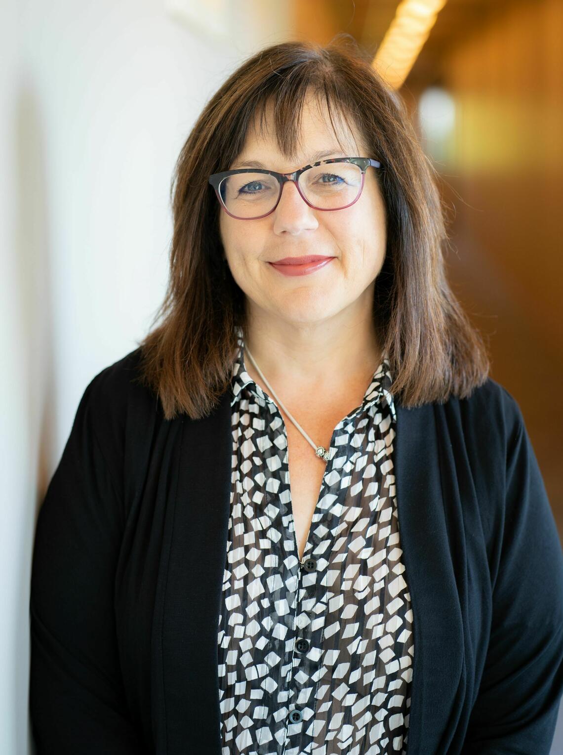 A woman with short brown hair and glasses smiles at the glasses