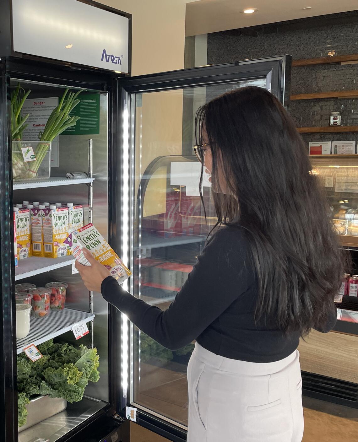 person looking at drink in her hand with open fridge full of produce and beverages