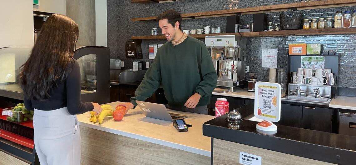 A person paying for produce at a till with the help of a cashier.