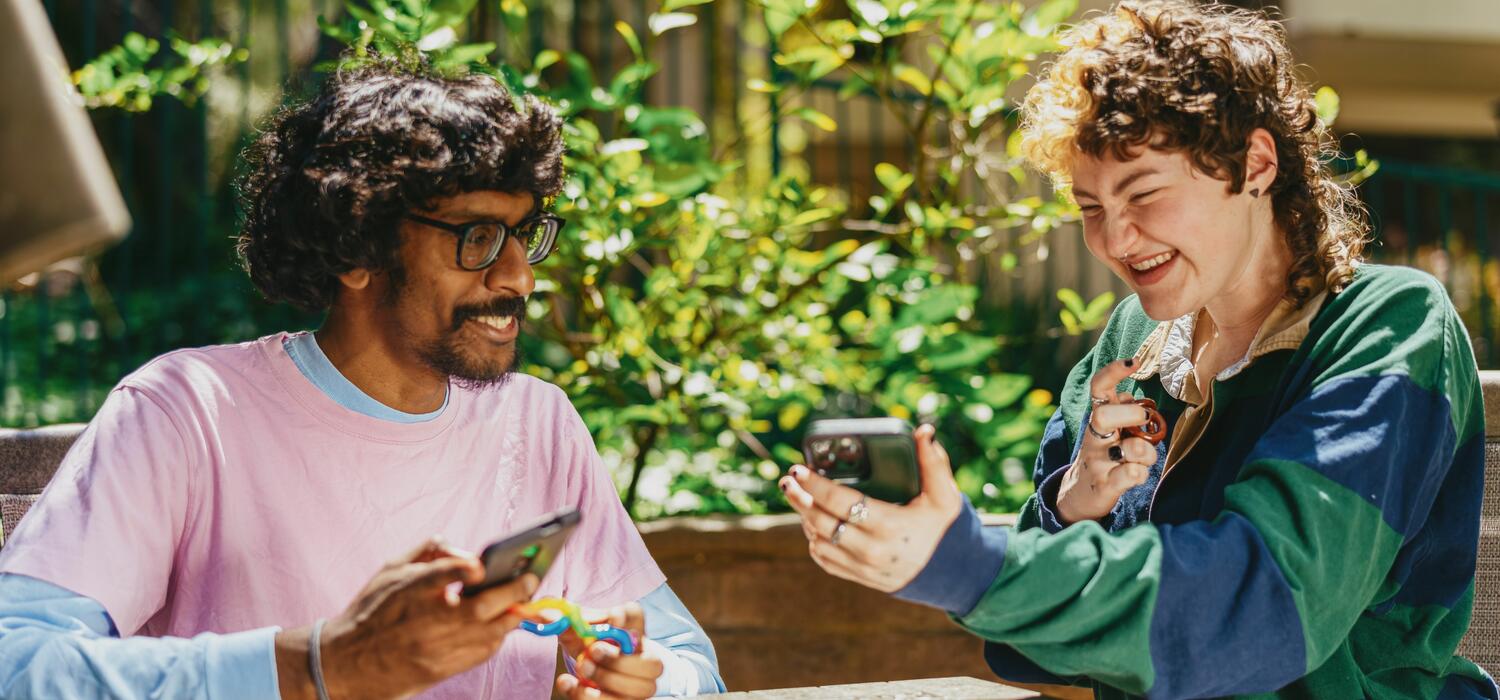 Two autistic friends sitting outside using stim toys and laughing at their phones