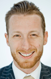 Alumnus Michael J. Burak smiles in close up. He is wearing a suit and standing against a white background