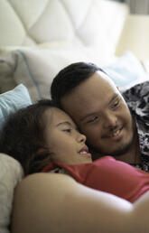 Two disabled people laying in a bed looking at mobile phone